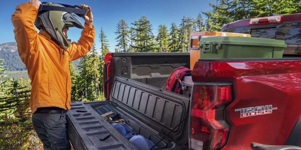 Homme ajustant son casque à côté d’un Chevrolet Colorado 2026 Trail Boss rouge chargé d’équipement d’aventure.