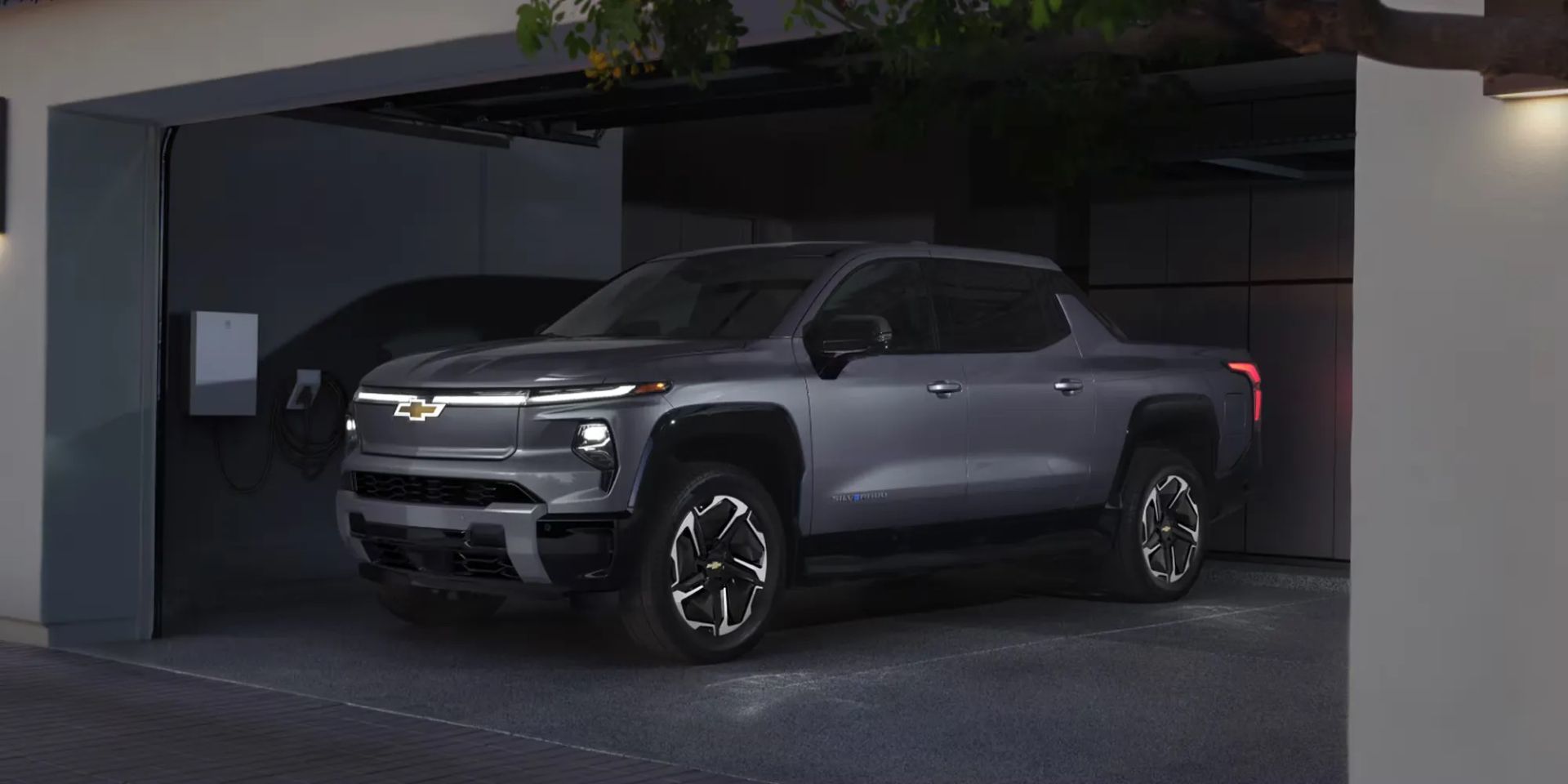 Chevrolet Silverado EV 2026 argenté garé dans un garage résidentiel, branché à une borne de recharge murale, illustrant sa motorisation électrique.