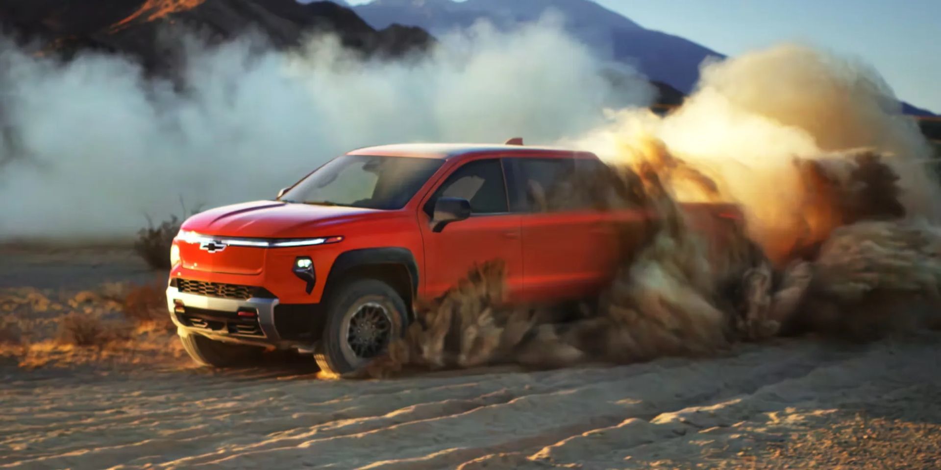 Chevrolet Silverado EV 2026 rouge projetant du sable dans le désert au coucher du soleil, illustrant sa puissance et ses capacités tout-terrain.