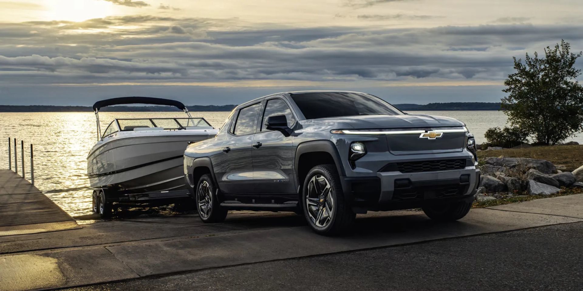 Chevrolet Silverado EV 2026 argenté garé près d’un quai avec un bateau au coucher du soleil, illustrant sa puissance de remorquage et son élégance.
