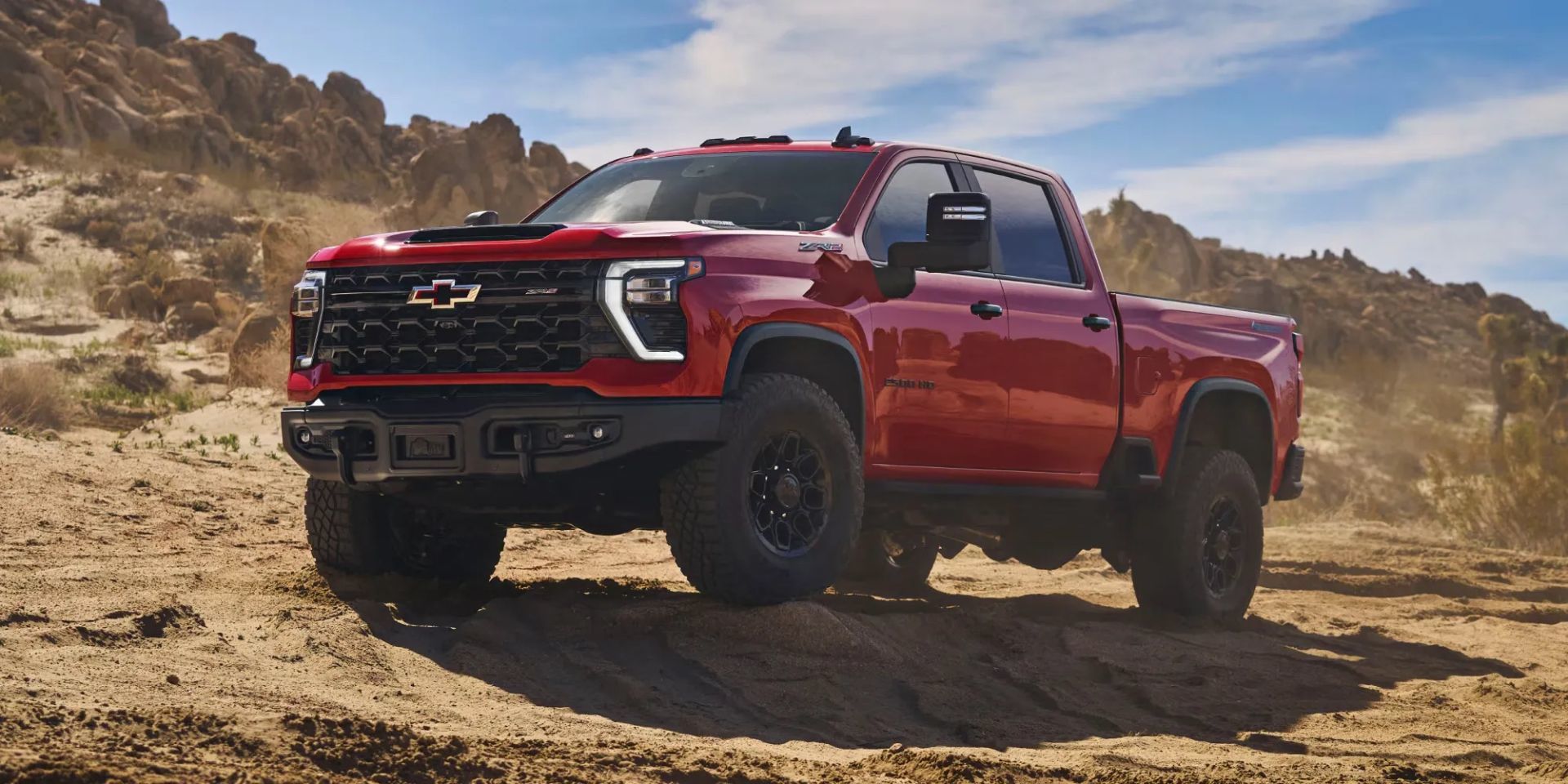 Chevrolet Silverado HD 2026 rouge sur un terrain sablonneux désertique, démontrant ses performances tout-terrain et sa puissance impressionnante.