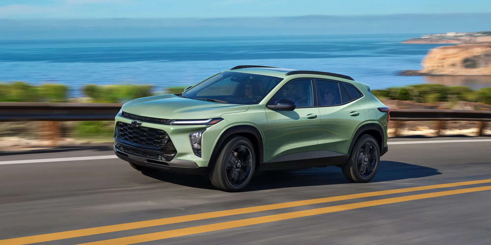 vue latérale avant d'un Chevrolet Trax 2026 vert roulant sur une route en bord de mer