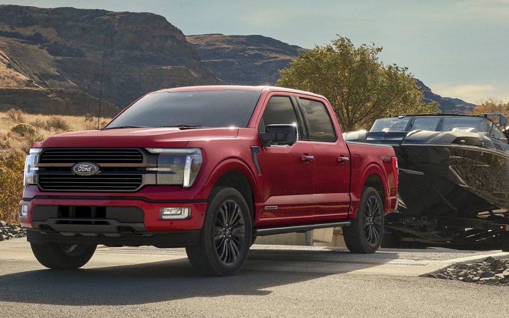 Camion Ford F-150 2025 rouge remorquant un bateau sur une route de montagne, illustrant la puissance et la polyvalence du modèle.
