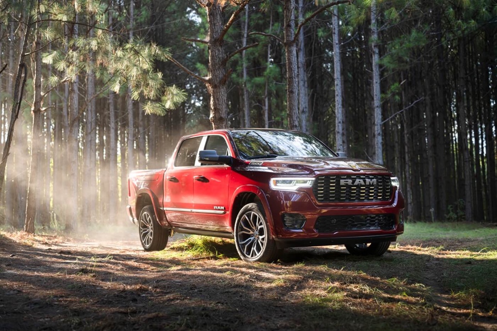 Ram 1500 2025 rouge circulant dans une forêt ensoleillée, illustrant sa robustesse et son confort haut de gamme.